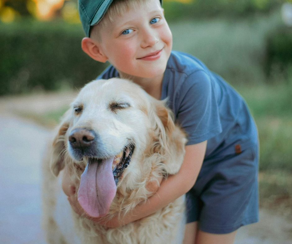 Niño abrazando a un perro Golden Retriever de pelaje claro, ambos sonrientes y felices al aire libre